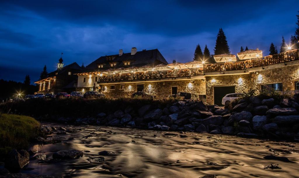 a house lit up at night next to a river at Pivovar Lyer in Modrava