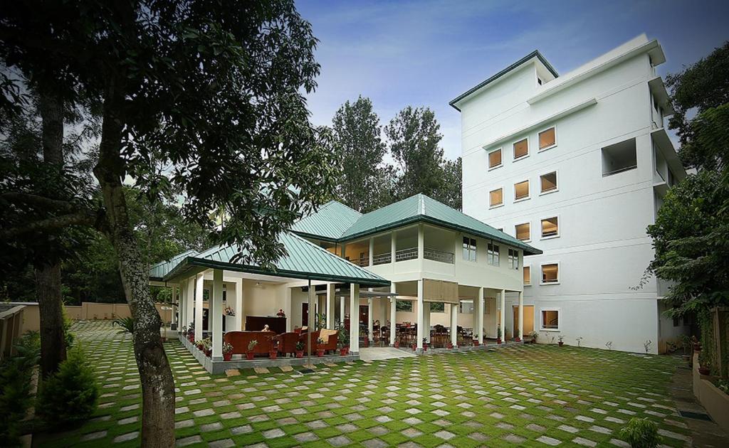 un grand bâtiment blanc avec une pelouse devant lui dans l'établissement Peppervine Hotel, à Thekkady