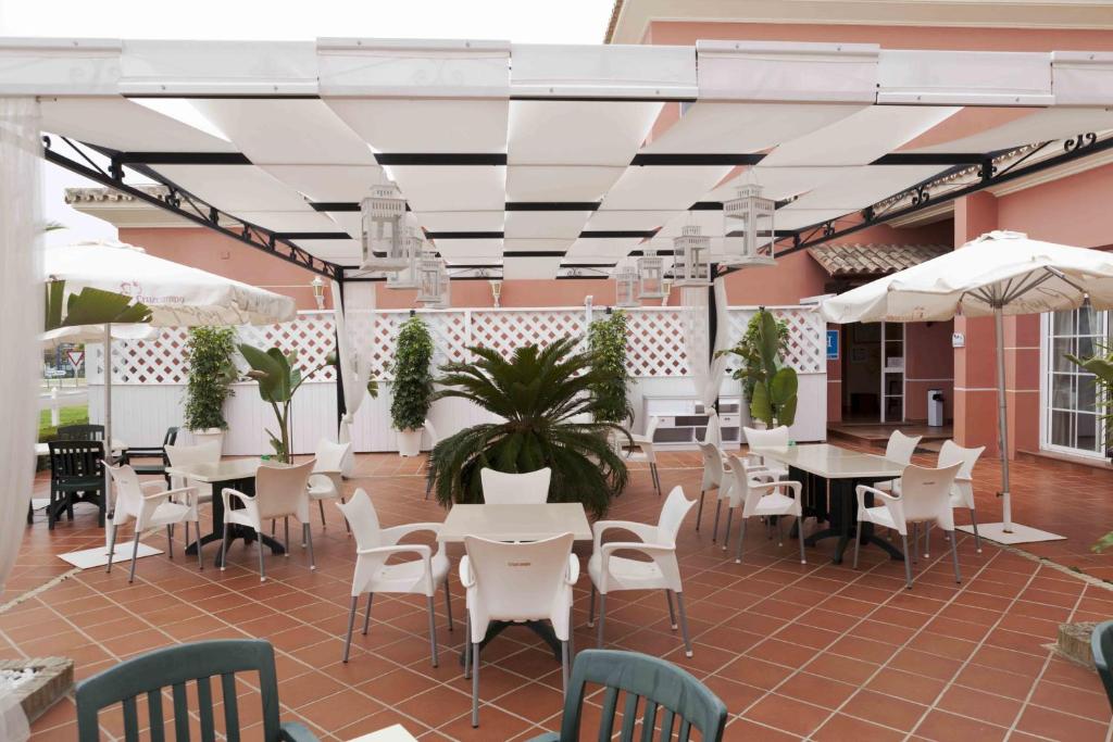 d'une terrasse avec des tables et des chaises blanches ainsi que des parasols blancs. dans l'établissement Hostal Rte. Casa Miguel, à Matalascañas