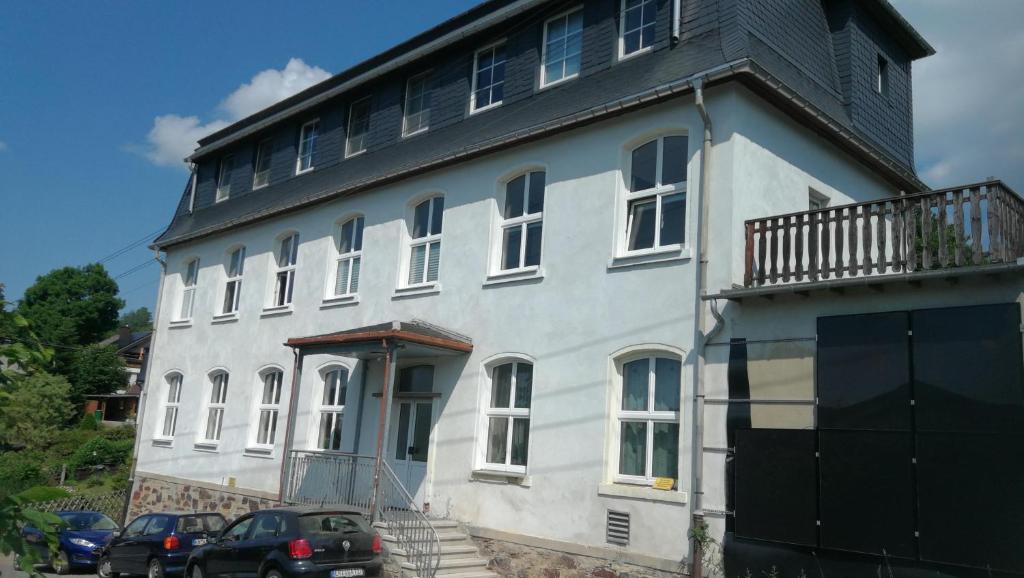 duży biały budynek z samochodami zaparkowanymi przed nim w obiekcie Ferienwohnung Sonnenblick w mieście Burkhardtsdorf