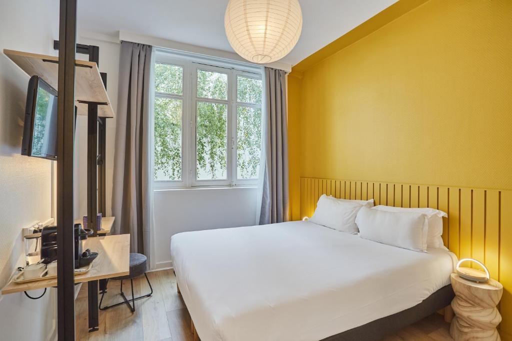 una camera con un letto bianco e una parete gialla di Hôtel Beauquartier Montmartre a Parigi