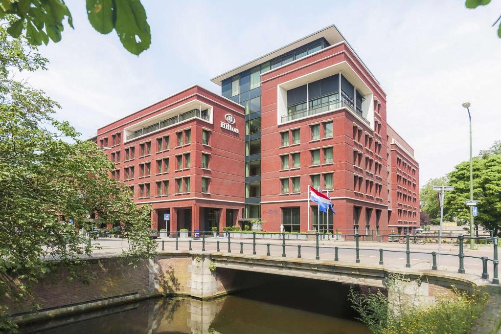 ein rotes Gebäude mit einer Brücke neben einem Fluss in der Unterkunft Hilton The Hague in Den Haag