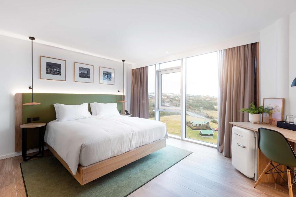 1 dormitorio con cama, escritorio y ventana grande en Hilton Garden Inn Faroe Islands, en Tórshavn