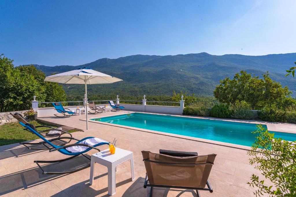 uma piscina com cadeiras, uma mesa e um guarda-sol em Villa Luce em Omiš