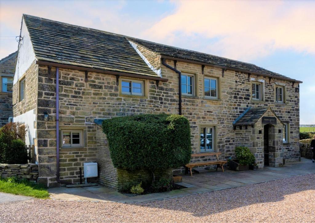 uma velha casa de pedra com um arbusto em frente em Thornes Cottage em Huddersfield