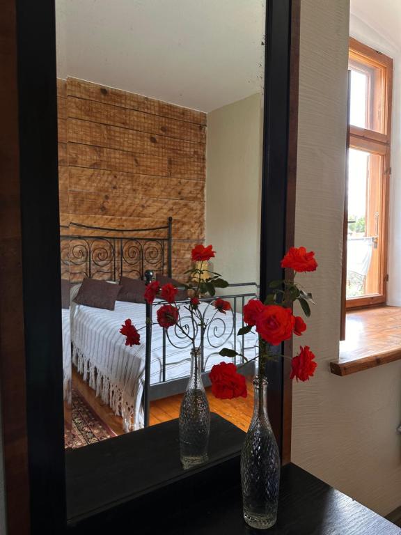 dos jarrones con flores rojas en una mesa frente a un espejo en Baznīcas ielas apartamenti, en Kuldīga