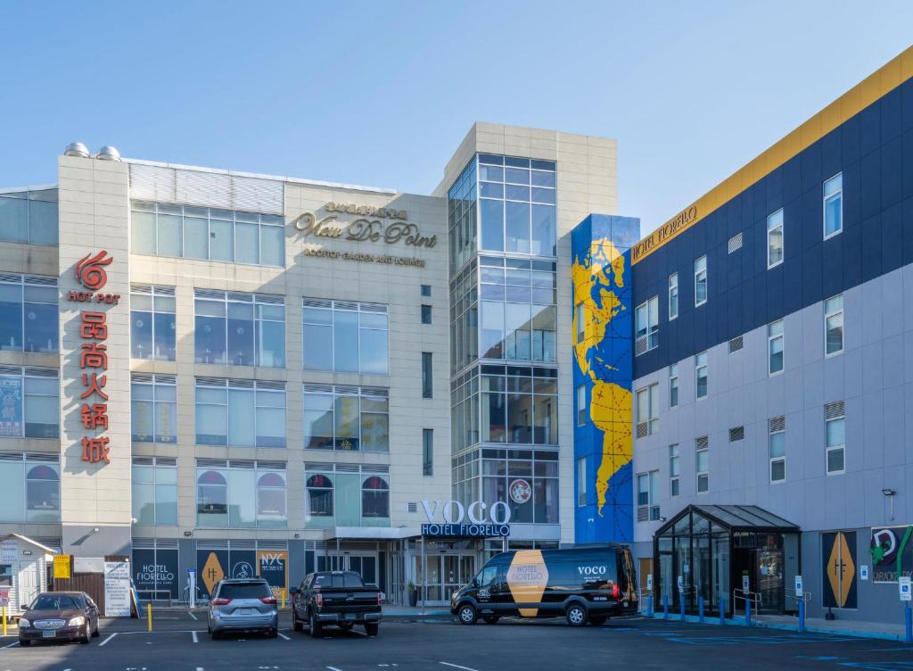 een groot gebouw met auto's geparkeerd op een parkeerplaats bij voco Fiorello - LaGuardia East, an IHG Hotel in Queens