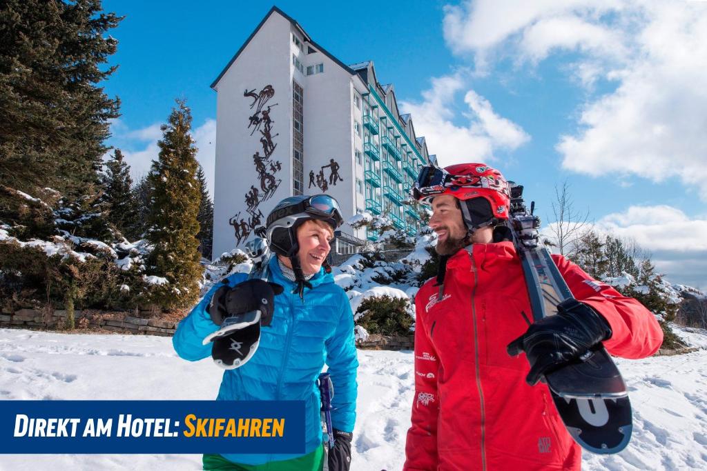 dois homens parados na neve em frente a um hotel em Best Western Ahorn Hotel Oberwiesenthal – Adults Only em Kurort Oberwiesenthal