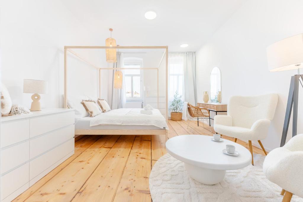 a white bedroom with a bed and a chair at Gran.Suite - Central Station in Sankt Pölten