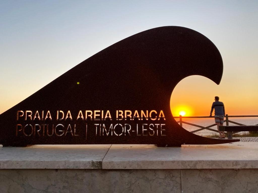 Ein Mann steht vor einer Skulptur mit Sonnenuntergang. in der Unterkunft Villa Surf Vista - Praia da Areia Branca in Lourinhã