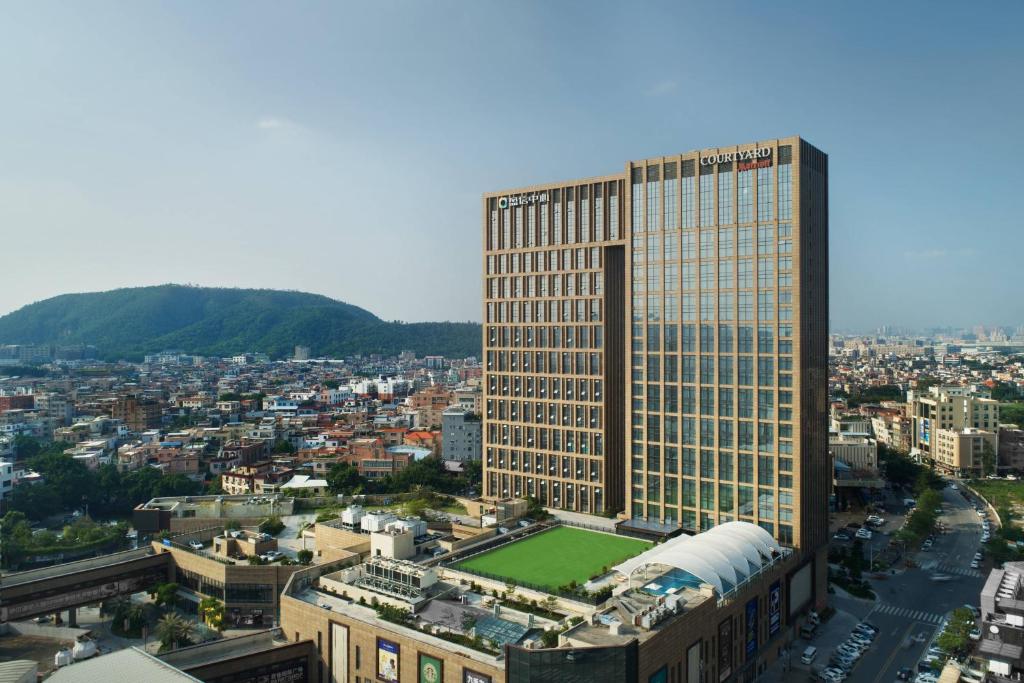 un grand bâtiment avec un champ vert en face d'une ville dans l'établissement Courtyard by Marriott Shunde Longjiang, Near Lecong, à Shunde