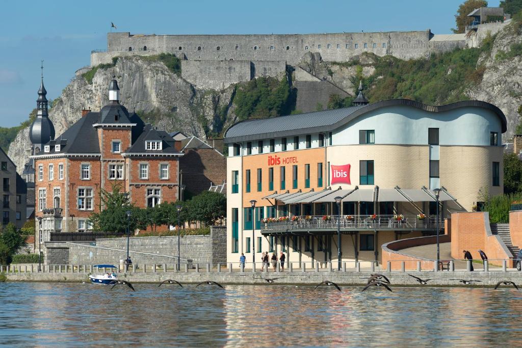 a building next to the water with a castle in the background at ibis Dinant Centre in Dinant