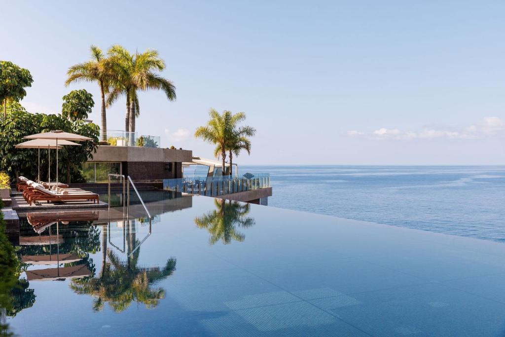 una piscina vicino all'oceano con palme di Saccharum - Resort and Spa - Savoy Signature a Calheta