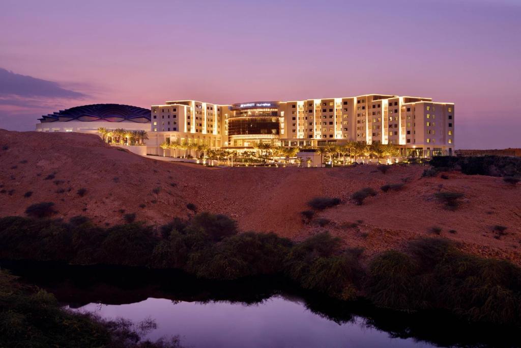 un grande edificio in cima a una collina di notte di JW Marriott Hotel Muscat a Mascate