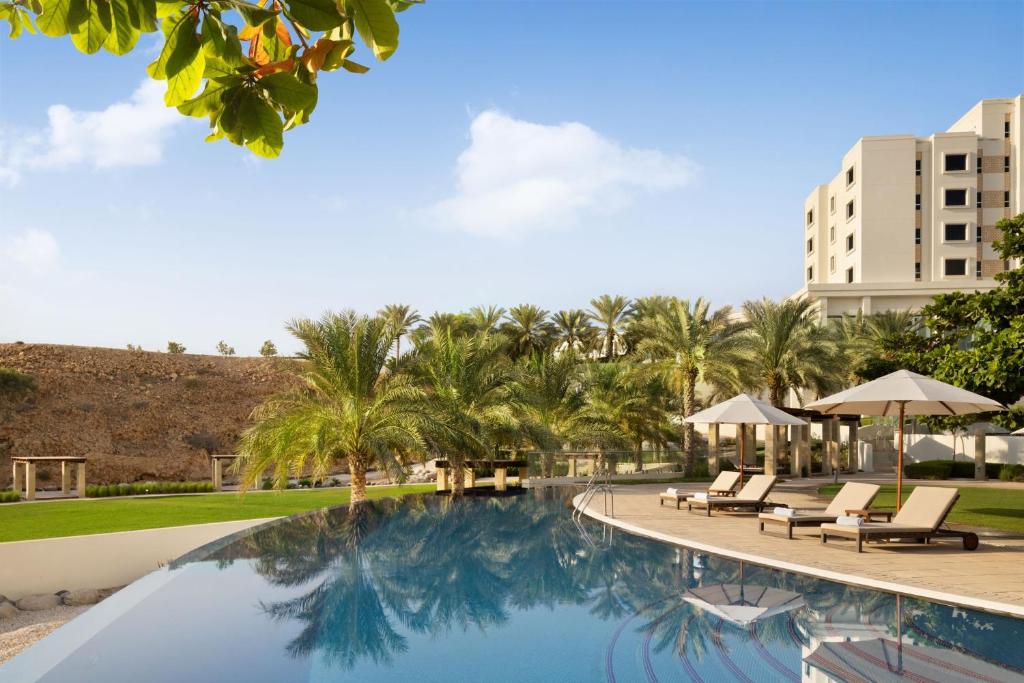 una piscina en un complejo con sillas y palmeras en JW Marriott Hotel Muscat, en Mascate