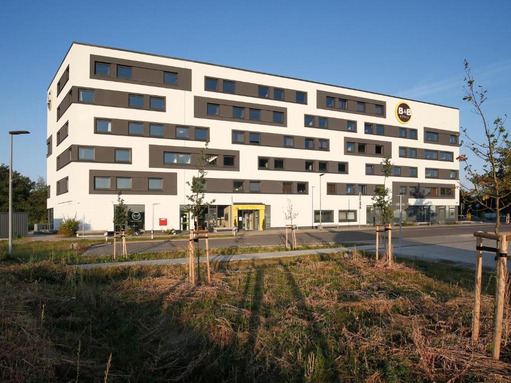 un bâtiment blanc avec des arbres devant lui dans l'établissement B&B Hotel Berlin-Airport, à Schönefeld