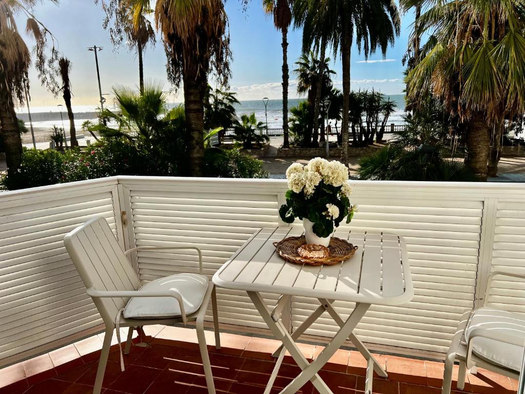 une table et des chaises blanches avec un vase de fleurs dans l'établissement Sitges Seafront Ribera Apartment, à Sitges