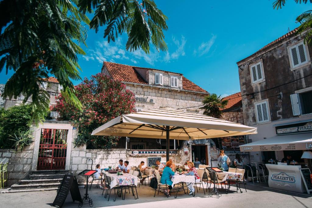 eine Gruppe von Menschen, die unter einem Schirm an Tischen sitzen in der Unterkunft Guesthouse Mimbelli in Orebić