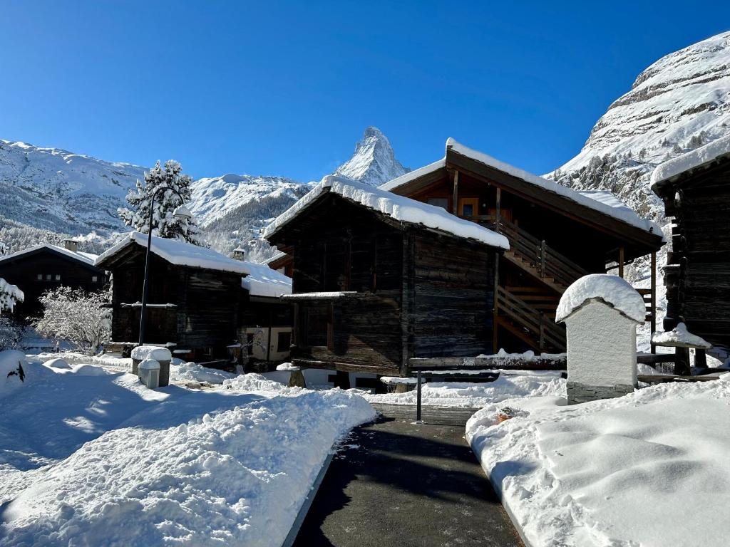 eine schneebedeckte Hütte mit Bergen im Hintergrund in der Unterkunft Chalet Coral und Zermatter Stadel mit Sauna in Zermatt