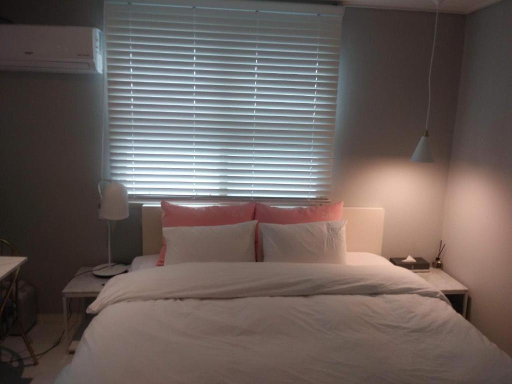 1 cama con sábanas blancas y almohadas rosas frente a una ventana en 해운대 모모쥬스호텔 부산 MoMo Juice Busan Haeundae, en Busan