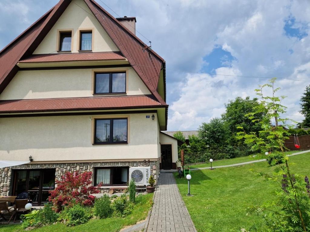 uma casa com um telhado vermelho e um jardim de relva em Pokoje Gościnne u Cześka em Kluszkowce