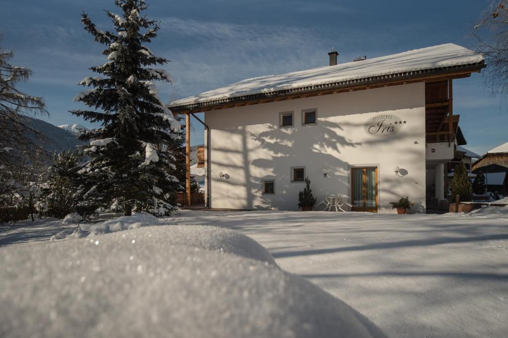 een besneeuwd huis met een kerstboom ervoor bij Residence Iris in Valdaora