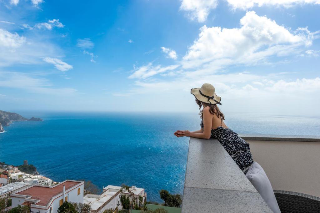 een vrouw die op een richel zit en uitkijkt op de oceaan bij Albadamare Boutique Hotel in Praiano