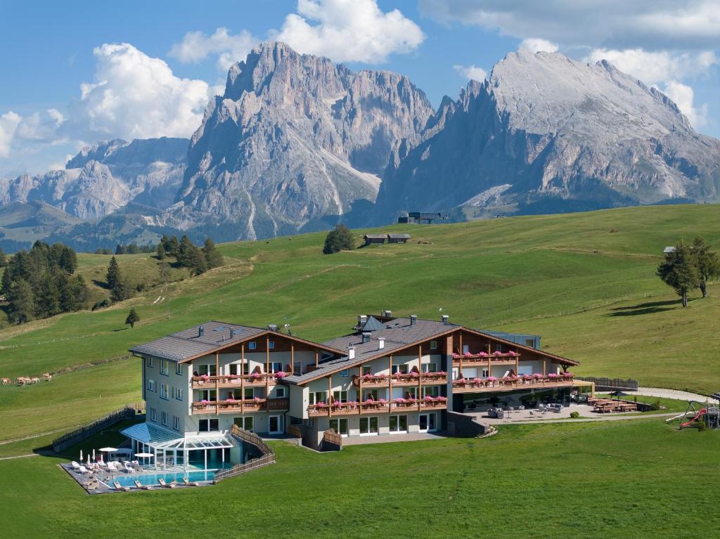 ein Hotel auf einem Hügel mit Bergen im Hintergrund in der Unterkunft Hotel Santner Alpine Sport & Relax in Alpe di Siusi