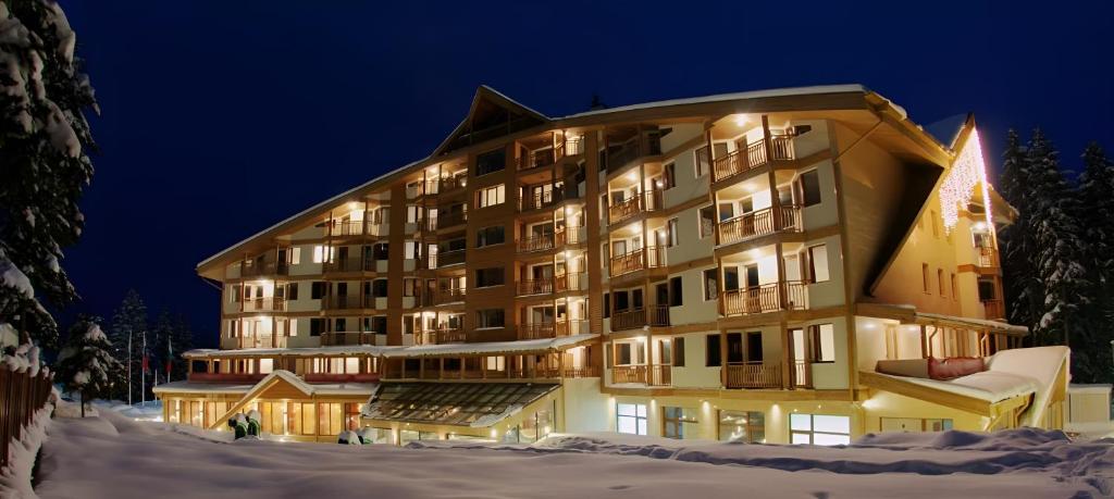 un grand bâtiment dans la neige la nuit dans l'établissement Hotel Iceberg Borovets, à Borovets