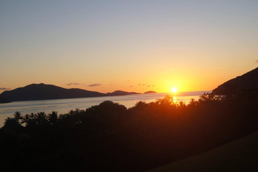 einen Sonnenuntergang über dem Wasser mit Bergen im Hintergrund in der Unterkunft Poinciana 106 in Hamilton Island