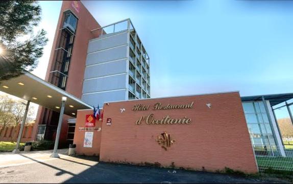 un bâtiment avec un panneau sur son côté dans l'établissement Hôtel Restaurant d'Occitanie, à Toulouse