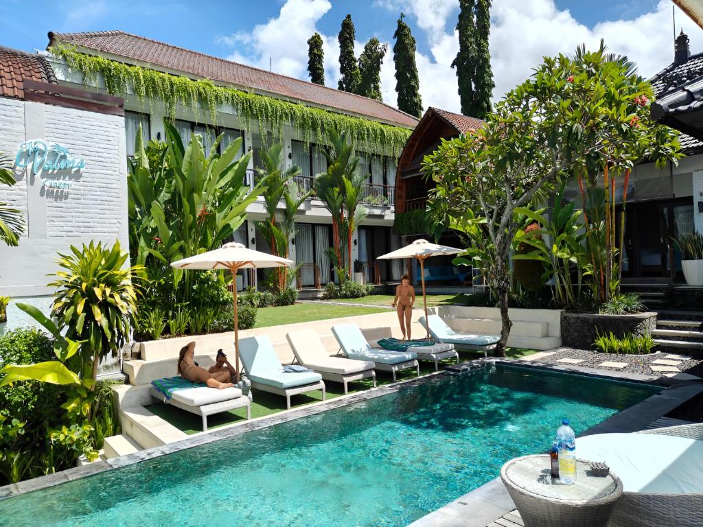 una piscina con tumbonas y sombrillas junto a un edificio en The Palms Canggu, en Canggu