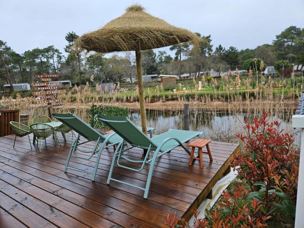 un groupe de chaises et un parasol sur une terrasse en bois dans l'établissement Mobil home tout confort au Camping Les Viviers, Cap Ferret, à Claouey