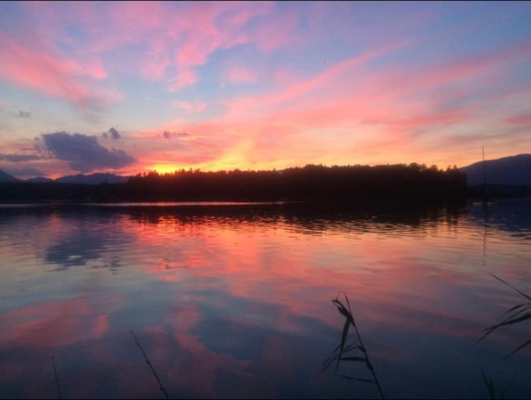 un coucher de soleil sur une étendue d'eau plantée d'arbres dans l'établissement Faakersee Seahouse mit Privat Strand -Only Sa-Sa, à Faak am See