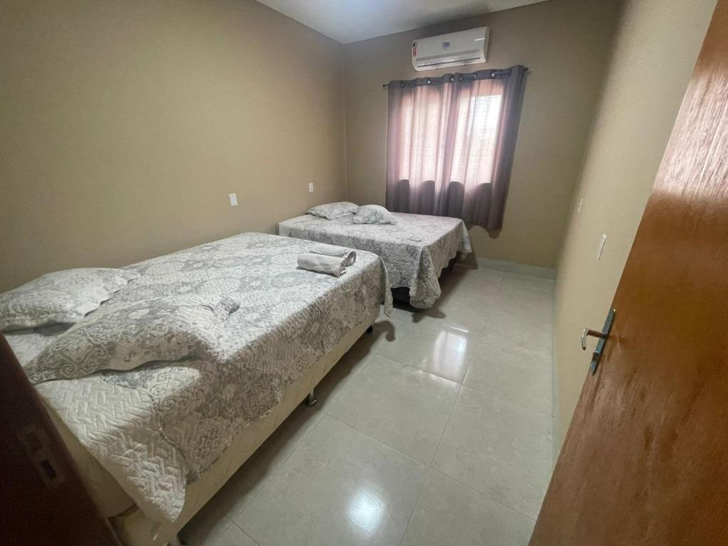 a bedroom with two beds and a window and a door at Casa de 2 quartos com ar, banheiros, pátio, mobília, tudo privativo - Projeto Suítes que Desconta duração e entra 15h adiante inclusive à noite in Sorriso