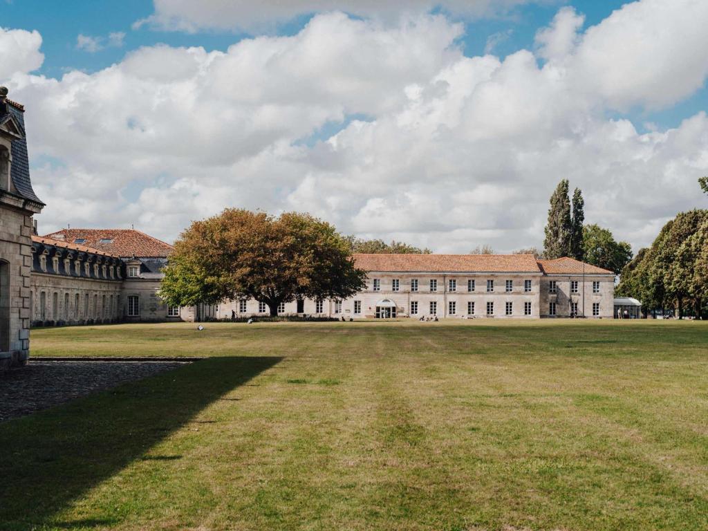 um grande edifício com um campo de relva em frente em Hôtel Mercure Rochefort La Corderie Royale em Rochefort