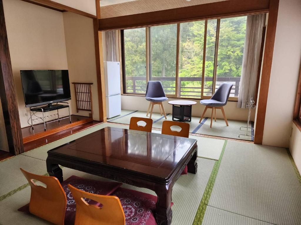 een woonkamer met een tafel en stoelen en een televisie bij 大和屋ホテルいろは in Nikko