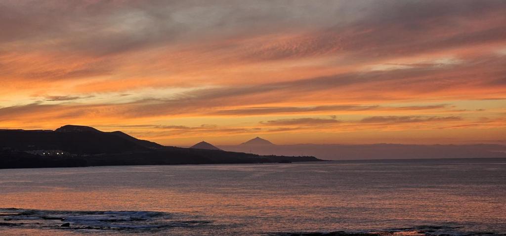 una puesta de sol sobre el agua con montañas en el fondo en Estudio 609 Playa Las Canteras doble, en Las Palmas de Gran Canaria