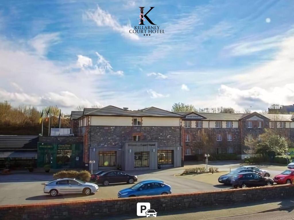 um grande edifício de tijolos com carros estacionados num parque de estacionamento em Killarney Court Hotel em Killarney