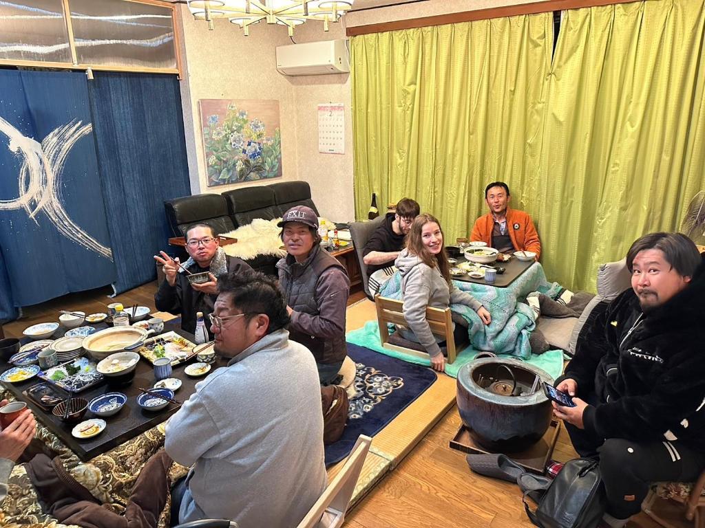 un gruppo di persone seduti intorno a un tavolo in una stanza di Guesthouse Oomiya base 大宮基地別荘 a Chiba