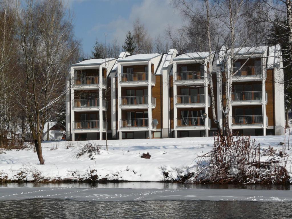 un immeuble dans la neige à côté d'une rivière dans l'établissement Apartamenty Wiślany Brzeg, à Ustroń