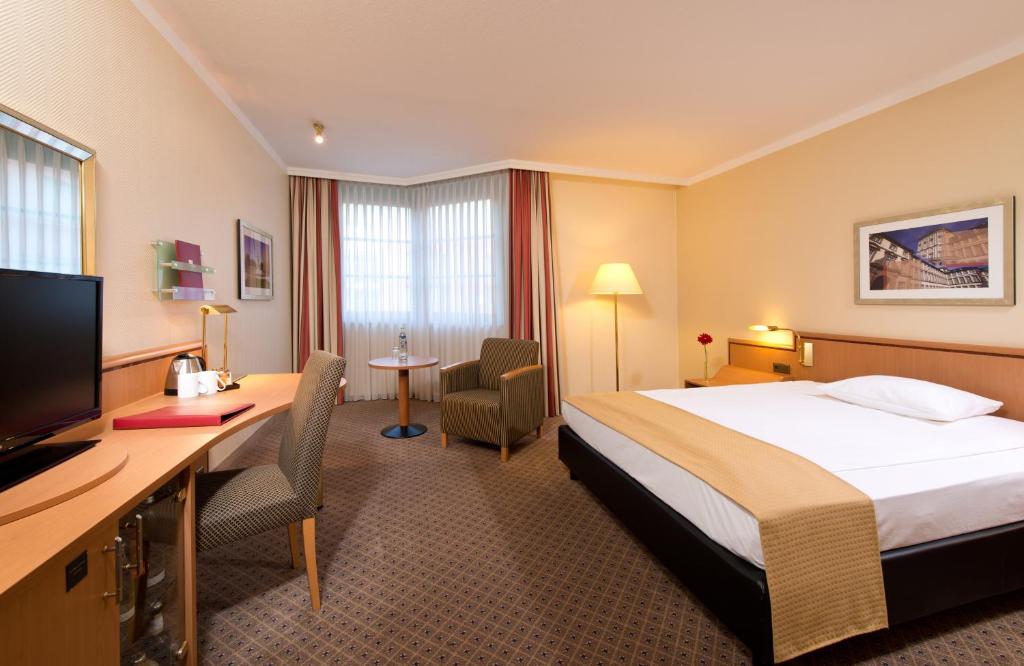 a hotel room with a bed and a desk at Leonardo Hotel Mannheim City Center in Mannheim