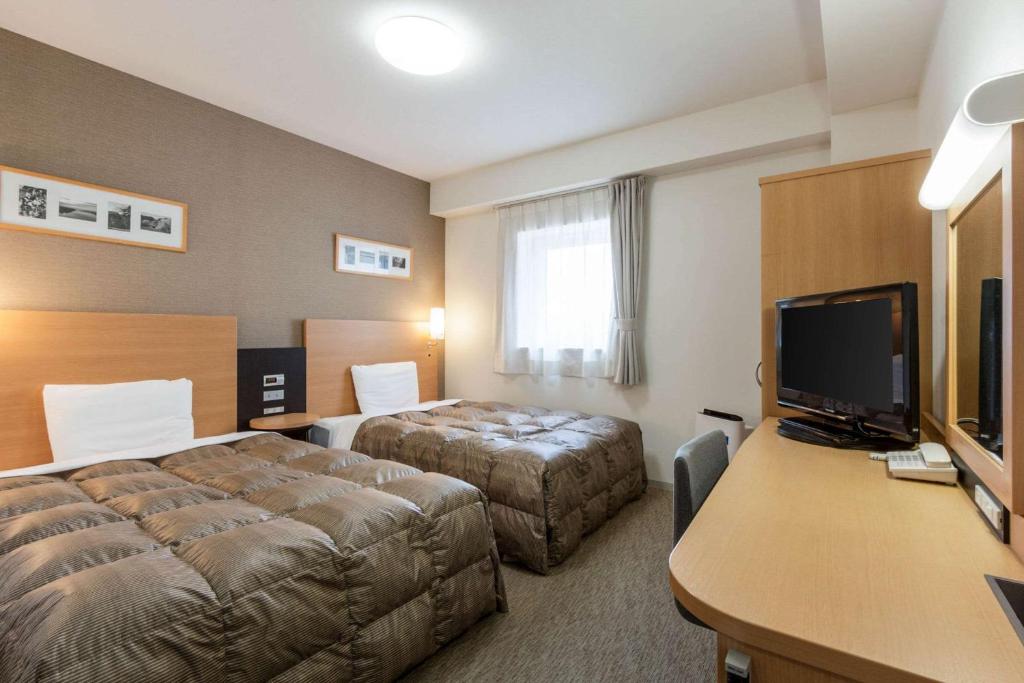 a hotel room with two beds and a desk at Comfort Hotel Kitakami in Kitakami