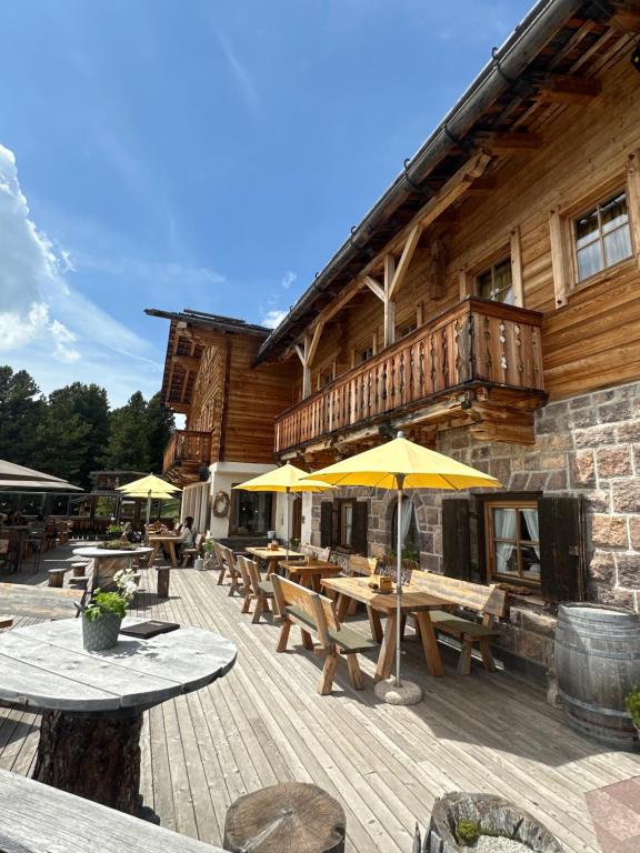 eine Holzterrasse mit Tischen und Sonnenschirmen vor einem Gebäude in der Unterkunft Chalet da mont Resciesa in St. Ulrich in Gröden