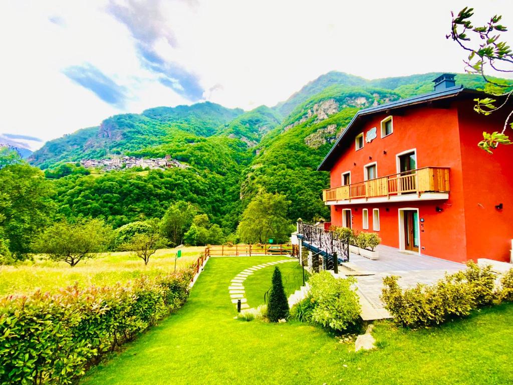 un edificio rosso in un campo con montagne sullo sfondo di Bed and Breakfast Soffio di Vento a Pont-Saint-Martin