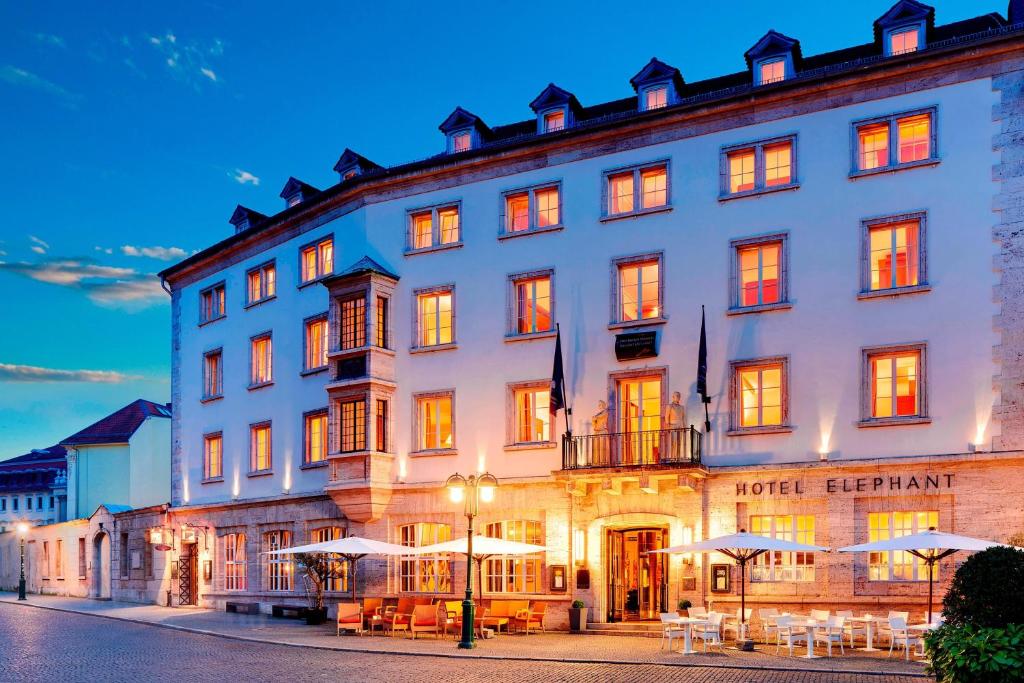 un grand bâtiment blanc avec des tables et des parasols dans l'établissement Hotel Elephant Weimar, Autograph Collection, à Weimar