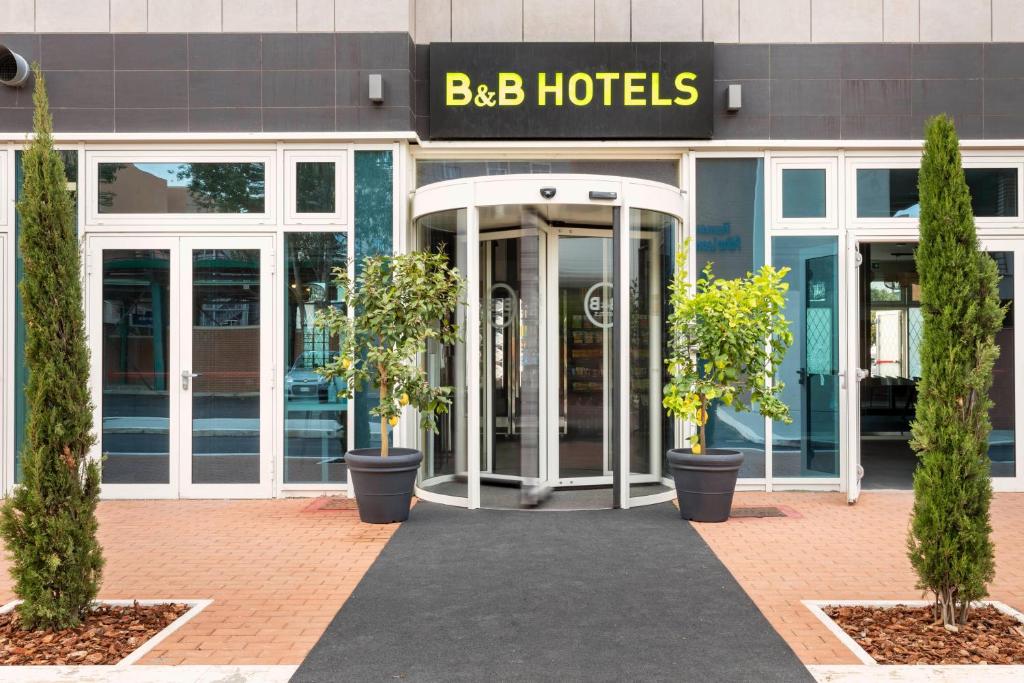 フィウミチーノにあるB&B Hotel Roma Fiumicino Aeroporto Fiera 2の鉢植えの木が目の前にあるホテルの入り口