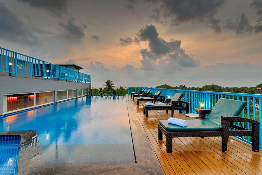 a hotel swimming pool with chairs and the ocean at De Mandarin Goa in Candolim