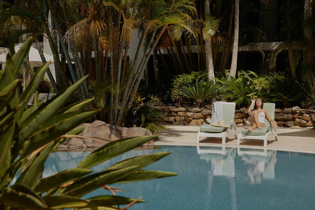 a woman sitting in chairs next to a swimming pool at The Executive Inn, Newcastle in Newcastle