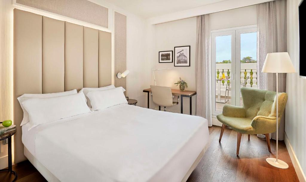 um quarto com uma grande cama branca e uma cadeira em NH Madrid Nacional em Madrid